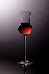 bright shining red liqueur in a shaft glass with refracting light and grey effusive background