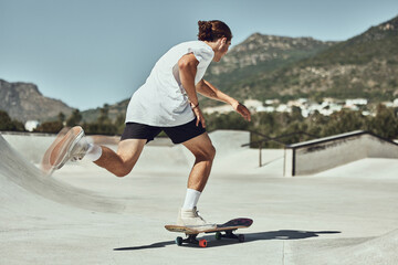 Skating, young man and skateboard at skate park in urban city, fitness or training for trendy...