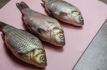 Three raw crucian fish on a cutting board	
