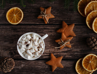 mug with marshmallows, ginger cookies with stars, orange slices, cones on a wooden background