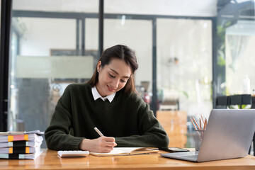 studying remotely from home, using a laptop, taking notes on notepad during online lesson, e-learning concept, smiling