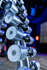 Rack with dumbbells shining in blue light in the gym. Sports and fitness room. Weight Training Equipment. Dumbbell set, many dumbbells on rack in sport fitness center. Barbells of different weights.