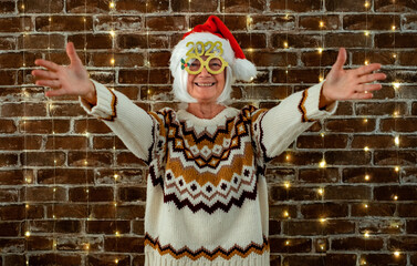 Happy senior caucasian woman with funny glasses and winter sweater looking at camera with open arms...