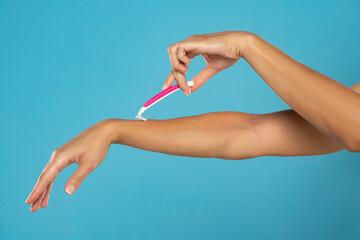 A woman shaves her arms with a disposable pink razor on a blue background