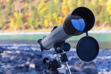 Naklejka premium Gray with black telescope stands on bank of mountain river in autumn, copy space, selective focus