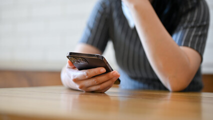 A woman holding her smartphone, using her mobile phone while sitting in the coffee shop.