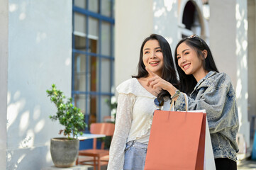 Attractive Asian woman pointing her finger at the clothes store, enjoys shopping with her friend