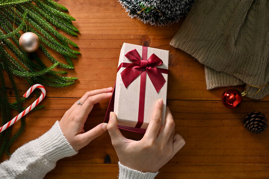 A Female Hands Opening A Surprise Christmas Gift Box Over Wooden Table With Christmas Decor.