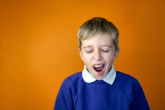 A tired school boy is yawning in school uniform, orange background, copy space