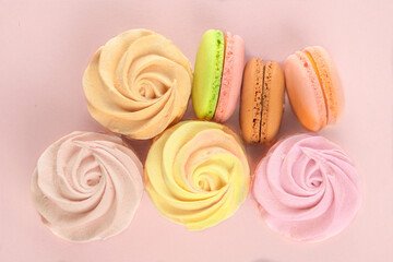 Sweet desserts for the holiday. Desserts: macaroons, marshmallows and zephyrs on a pink background, closeup. Top view.