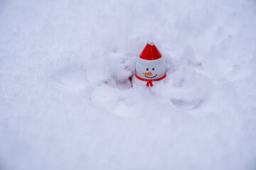 snowman with red hat sitting in snow. Christmas and new year winter holidays concept. White background, extreme cold weather 