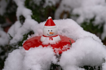 snowman toy with red hat sitting in snow. Christmas decoration on pine fir tree branch. New year winter festive holidays concept. Extreme cold weather 