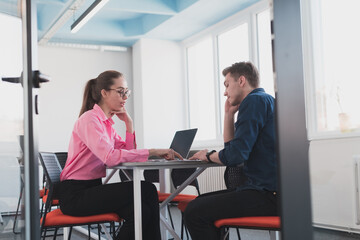 Two young entrepreneurs, a businessman and a businesswoman, sitting in a modern glass office and exchange business ideas