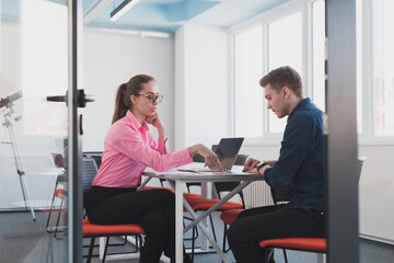 Two young entrepreneurs, a businessman and a businesswoman, sitting in a modern glass office and exchange business ideas