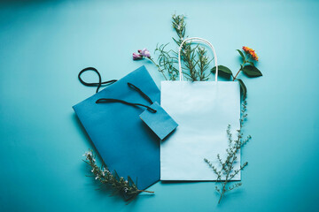 Seasonal mockup of a blue paper gift bag surrounded by flowers in flat lay format