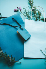 Seasonal mockup of a blue paper gift bag surrounded by flowers in flat lay format