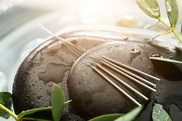 Acupuncture needles and spa stones in water, closeup