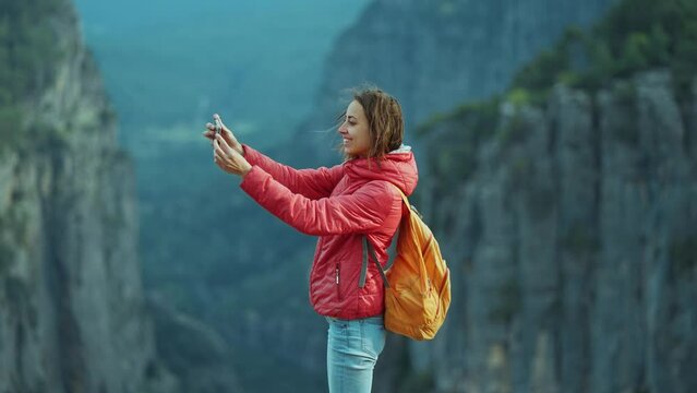 hiker at view point of Tazi Canyon. A girl takes pictures of stunning canyon landscape on her smartphone. Happy woman on top of cliff enjoying mountain view, hike in famous touristic place in Turkey.