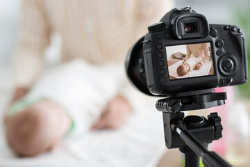 Young woman swaddling baby on screen of photo camera at home, closeup