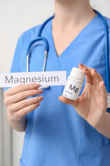 Female doctor with word MAGNESIUM and bottle of pills on light background, closeup