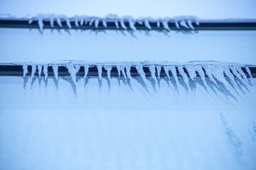 Icicles near the window in winter. Glazed facade of the building with icicles. Ice on windows in cold weather. Soft focus on ice icicle