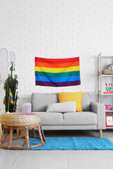 Comfortable sofa and rainbow flag hanging on white brick wall