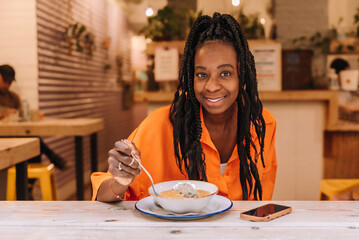 smiling afro american woman looking at the camera eating a vegetable cream. Healthy food concept