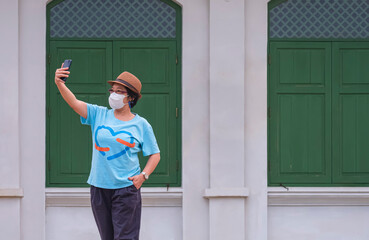 Female tourist in protective mask using smartphone to taking selfie while standing in front of vintage building wall