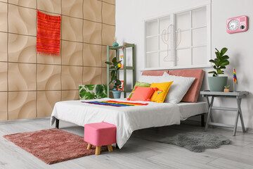 Comfortable bed with houseplants and rainbow flags in room