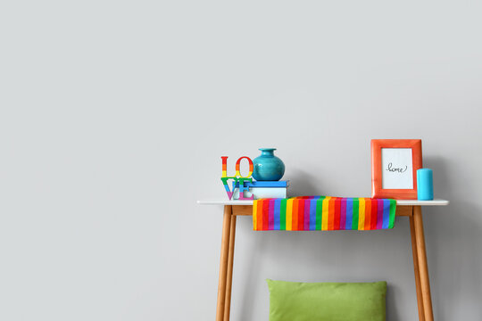 Rainbow flag, photo frame and vase on table near light wall