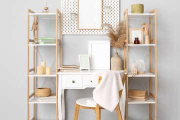 Modern workplace with blank frames, pegboard and shelving units near light wall