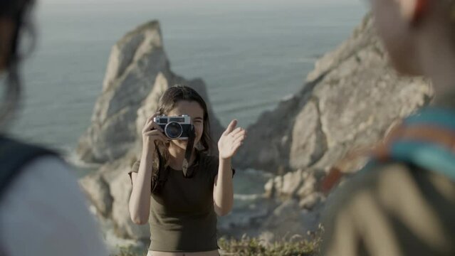Girl taking photo of her family while hiking in mountains. Caucasian teenager taking picture on cliff edge. Sea background. Blurred silhouettes in foreground. Front view. Photography, travel concept.