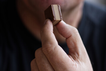 Mid age man holding chocolate candy close to his face, close up of hand.  
