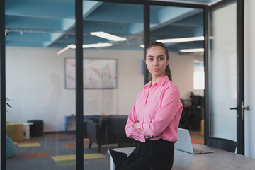 Fototapeta premium Portrait of young smiling business woman in creative open space coworking startup office. Successful businesswoman standing in office with copyspace. Coworkers working in background.