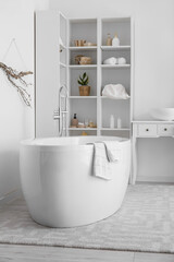 Modern bathtub and shelf units with bath accessories near white wall