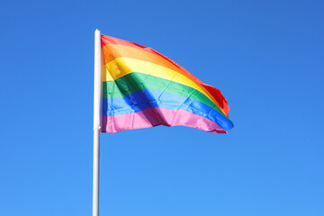 Waving LGBT flag against blue sky