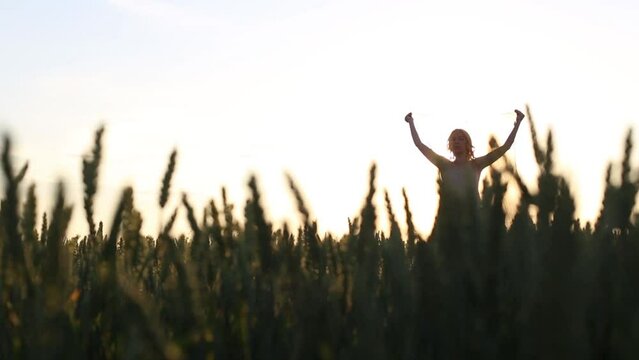 woman in the middle of a field greets the sun by raising her arms to the sky