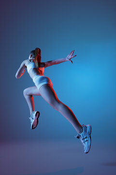 Back view of young sportive girl in white sportswear running away isolated over gradient blue purple background in neon light. Fitness, hobby, healthy lifestyle