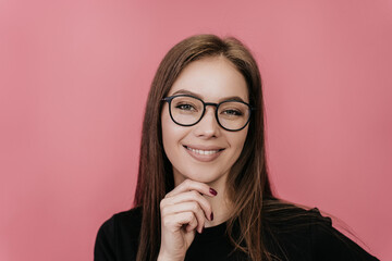 Close up portrait of smiling blonde young woman I glasses touching chin, looking at camera against pink background. Happy Swedish student girl broad smiling, received great news. Mockup, success.