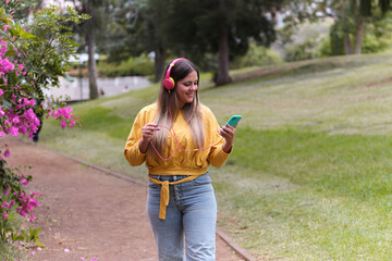 Young girl sitting on the grass with mobile phone headphones listening to music.