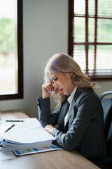 Portrait of a young Asian woman showing a serious face as she using financial documents and computer laptop on her desk in the early morning hours