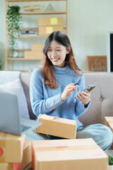 Starting small business entrepreneur of independent Asian woman smiling using computer laptop with cheerful success of online marketing package box items and SME delivery concept