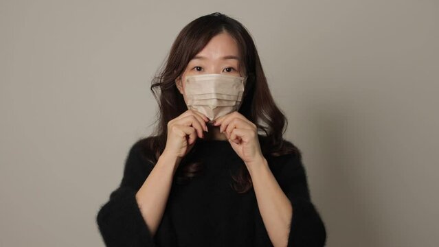 Asian woman put face mask on reluctantly. White background.