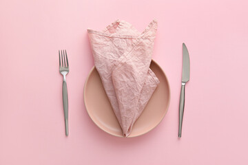 Table setting with napkin in plate and cutlery on pink background