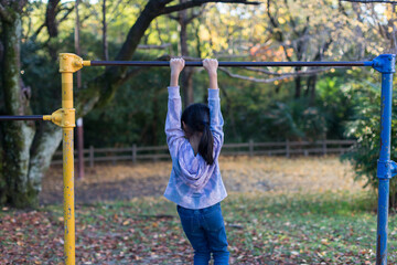 Fototapeta premium 秋の公園で鉄棒を遊んでいる小学生の女の子の姿