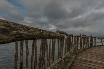 Long wooden pier with fence by Lake Constance with gray cloudy sky, Germany