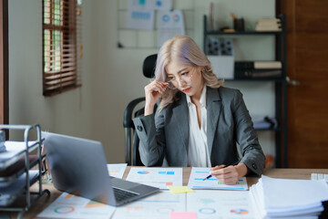 Portrait of a thoughtful Asian businesswoman looking at financial statements and making marketing plans using a computer on her desk