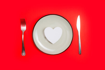 Romantic valentines day dinner idea concept. Heart on plate and silver wear on red background.