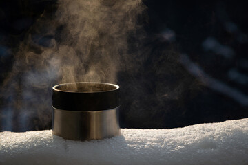 Close up of thermos cup with hot steaming drink outside on the snow. Nobody
