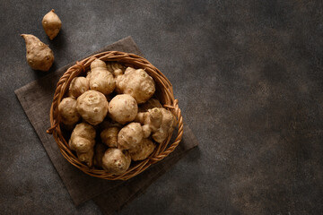 Raw Jerusalem artichoke root, sunchokes in wooden wicker basket and on brown background. View from...